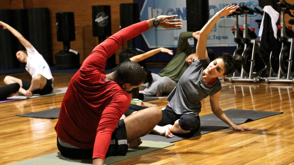 Symbolbild für Sport: Personen im Fitnessstudio, die sich mit Dehnübungen auf der Yogamatte bereitmachen.